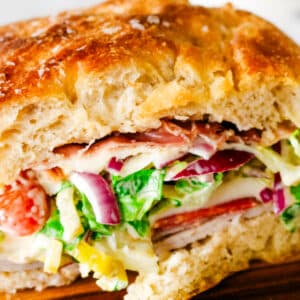 grinder sandwich on a focaccia bread with lettuce and red onions.