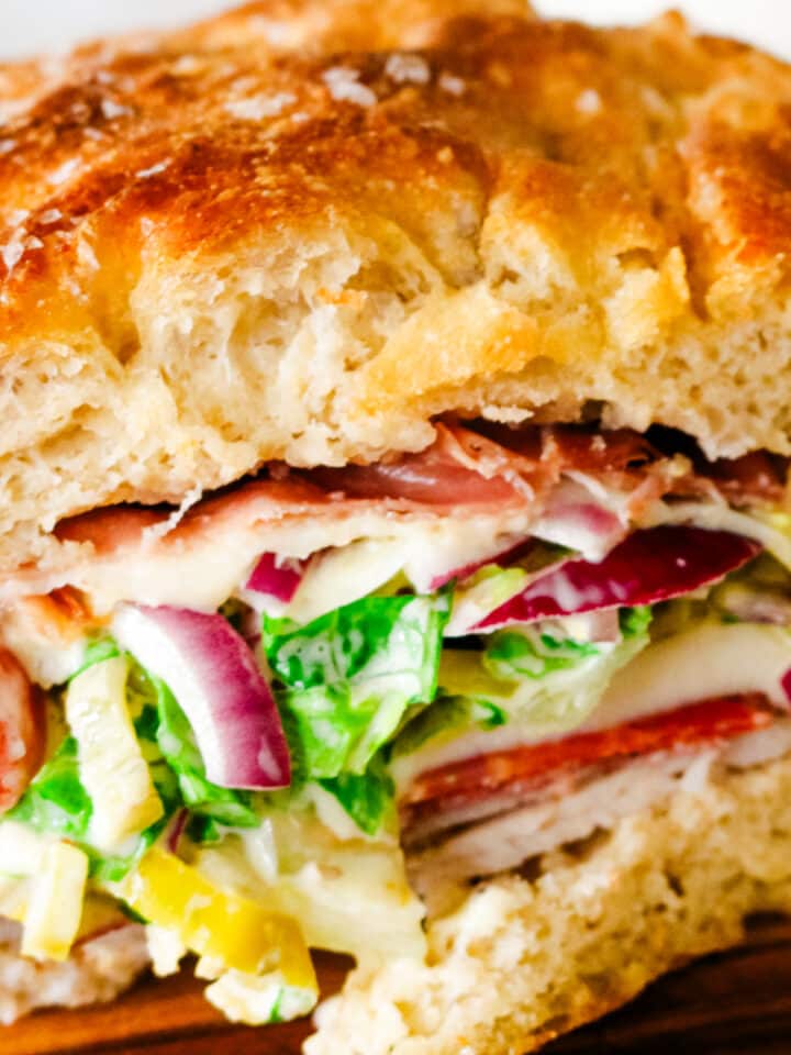 grinder sandwich on a focaccia bread with lettuce and red onions.