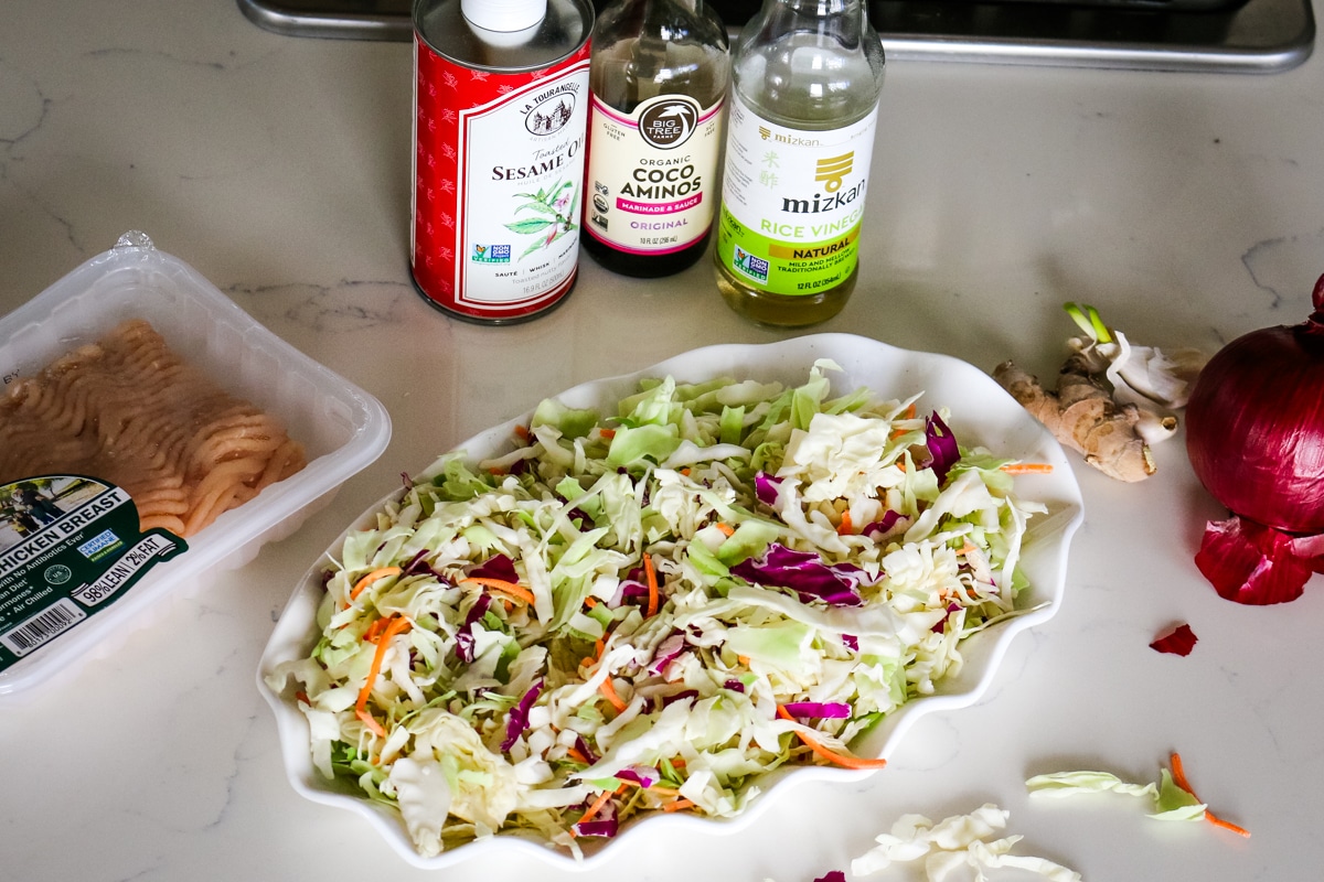 ingredients for egg roll in a bowl with rice vinegar, sesame oil, cabbage, and ground chicken.