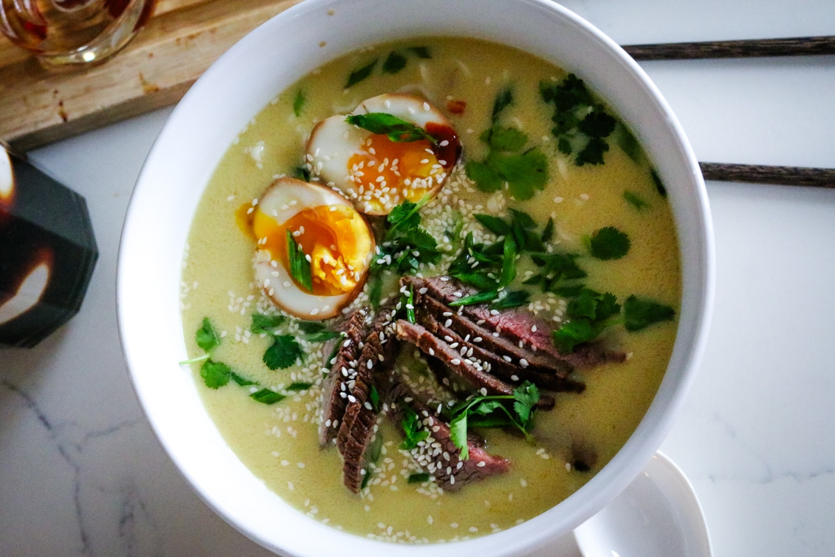 creamy ramen with soft-boiled eggs and steak in a white bowl.
