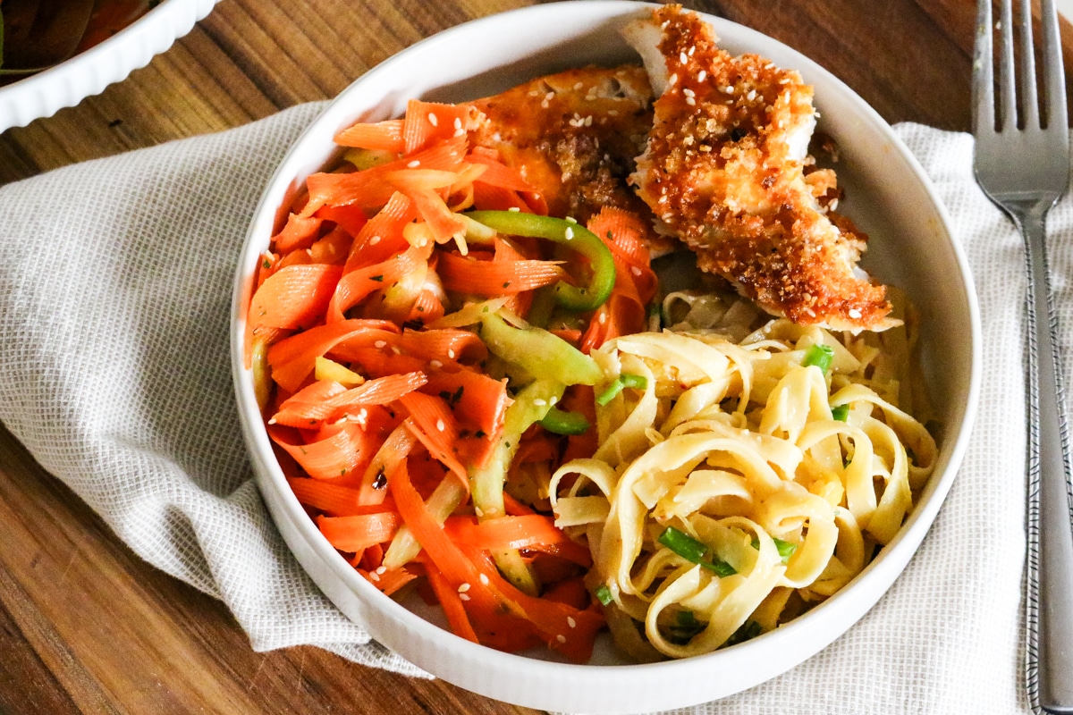 meal of shaved carrot salad, miso noodles, and panko crusted fish.