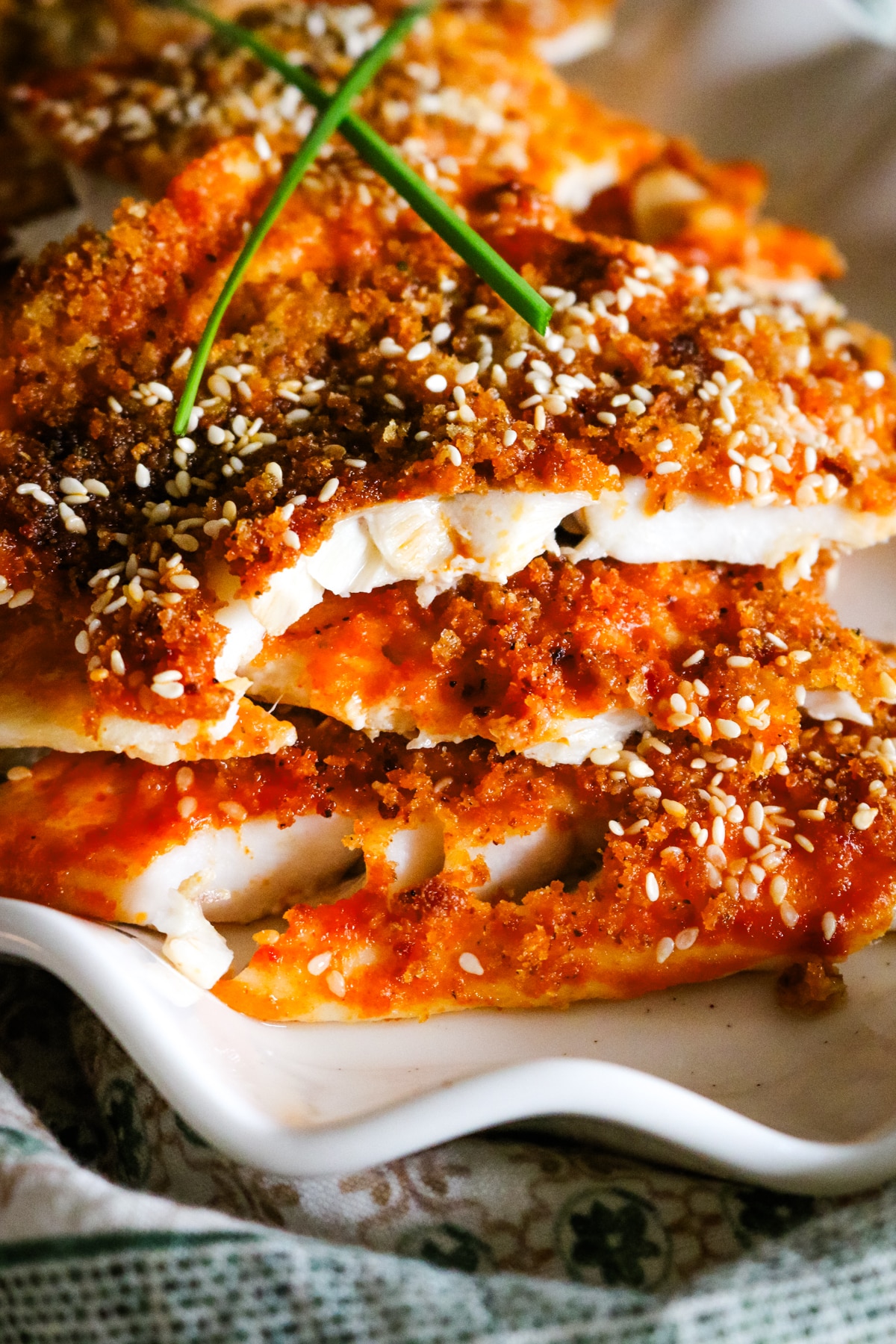 white fish crusted with spicy glaze and sesame seeds on a white platter.