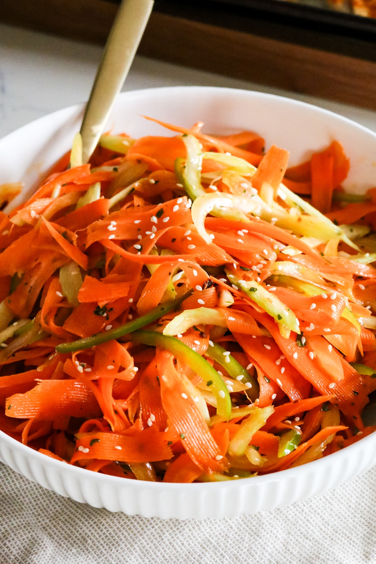 carrots shaved into ribbons in a white bowl with thin sliced bell peppers and celery.