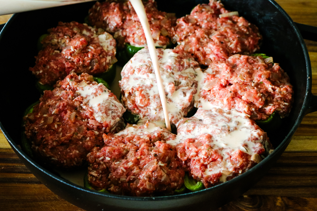 stuffed bell peppers being smothered by creamy tomato sauce