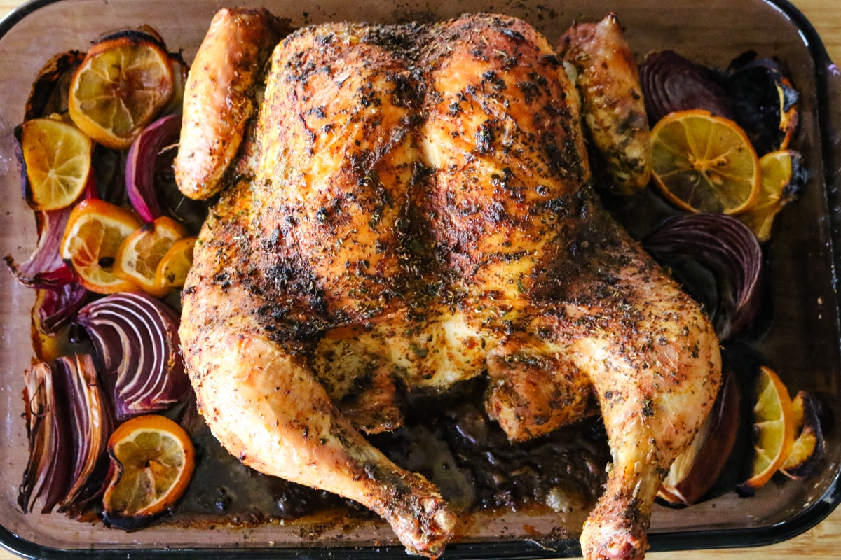 roast chicken in a baking dish with lemons and onions.