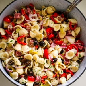 italian pasta salad in a white bowl with a spoon in the bowl.