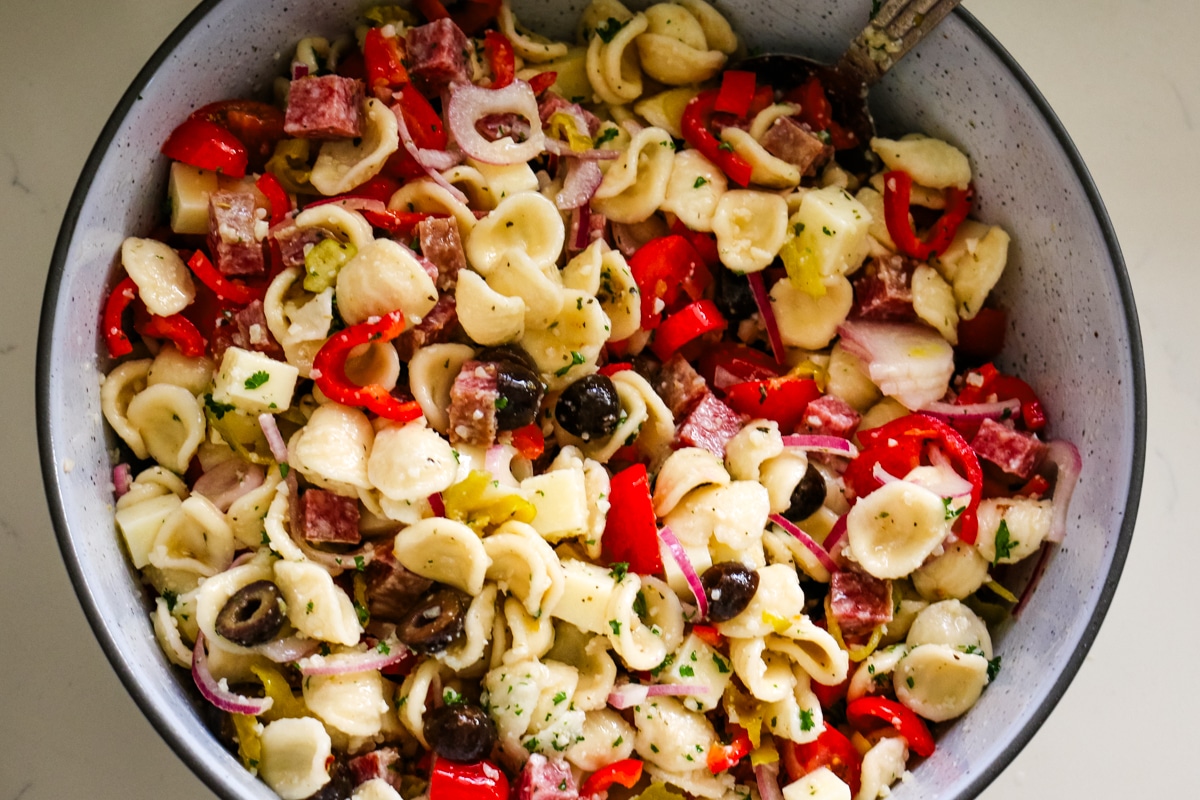 italian pasta salad in a white bowl with a spoon in the bowl.
