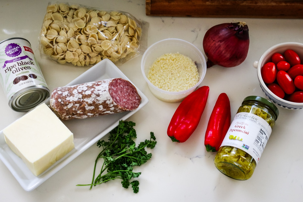 ingredients to make italian pasta salad layed out on a white counter.