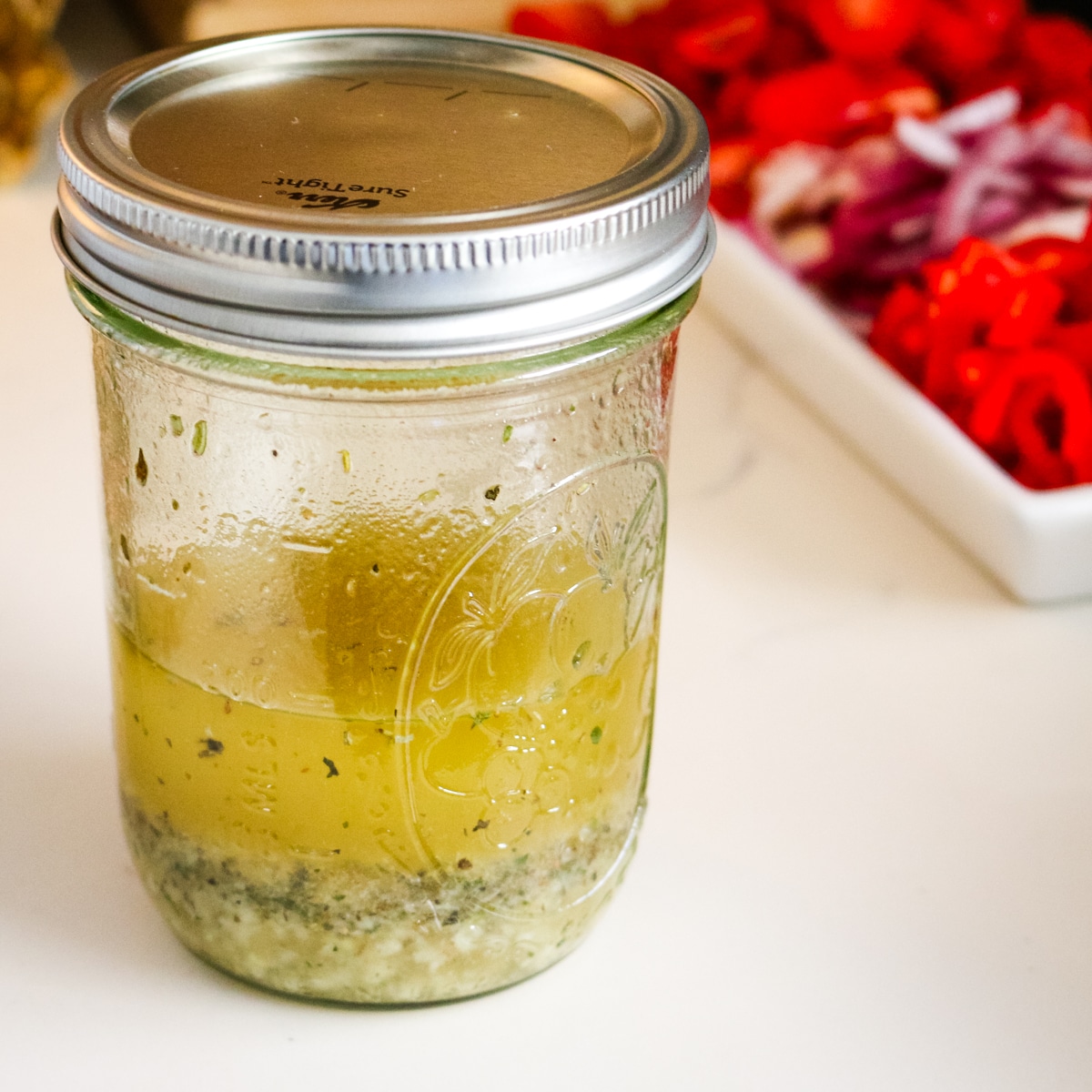 mason jar filled with italian pasta salad dressing with vegetables on a platter in the background.