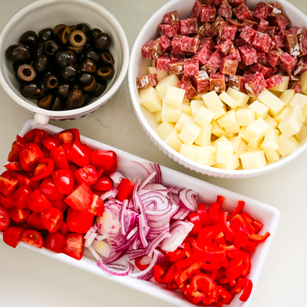 ingredients to make a italian pasta salad in bowls on a counter.
