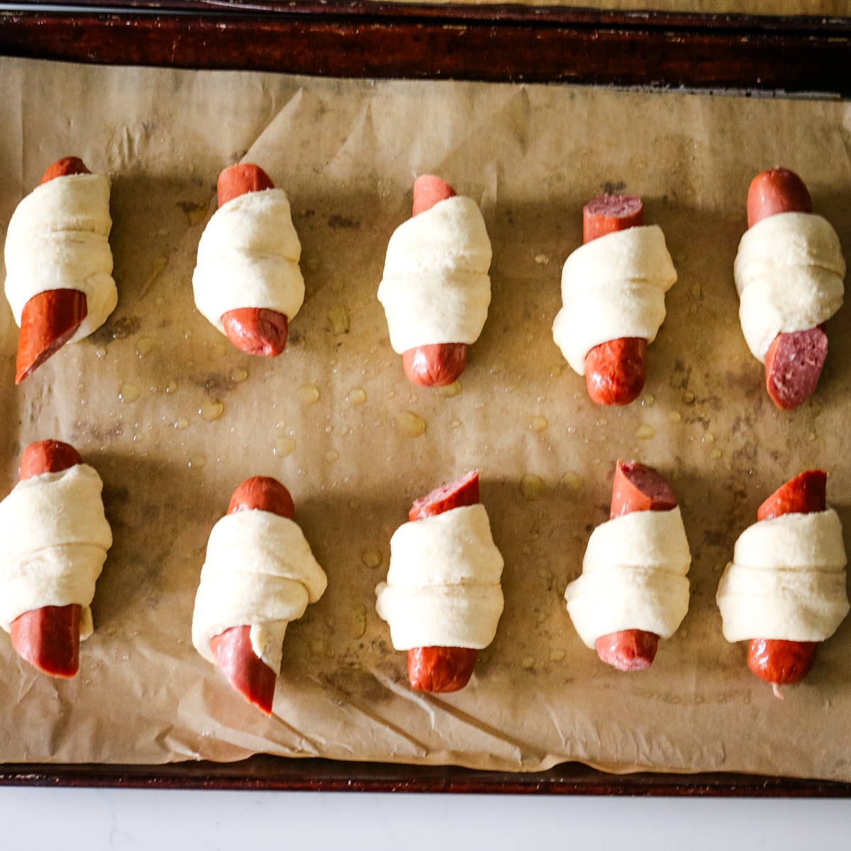 uncooked pigs in a blanket on metal pan.