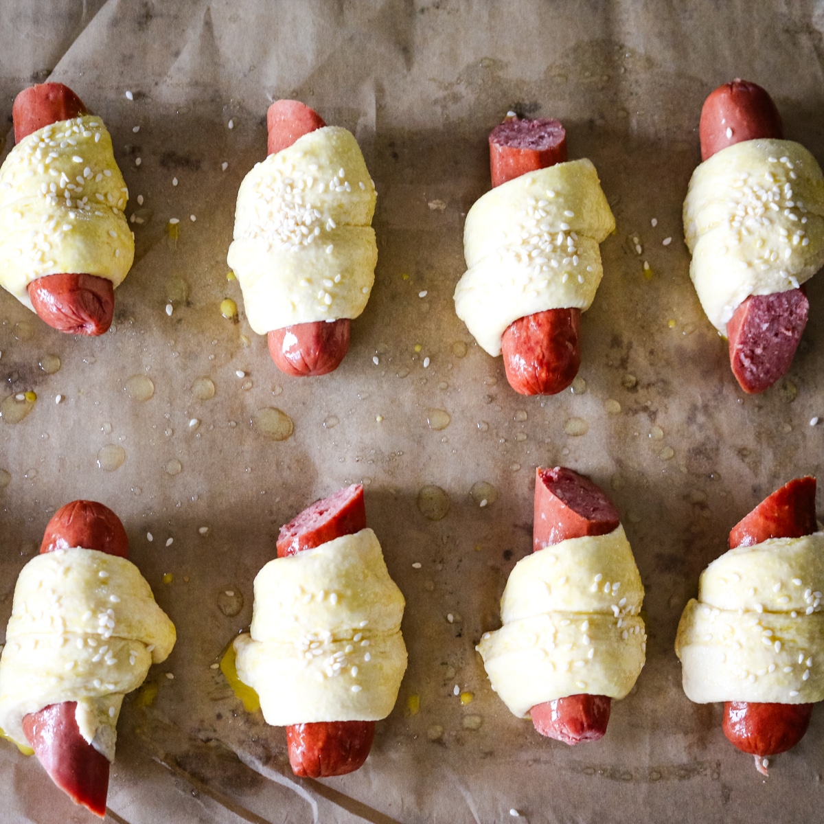 uncooked pigs in a blanket on parchment paper with oil.