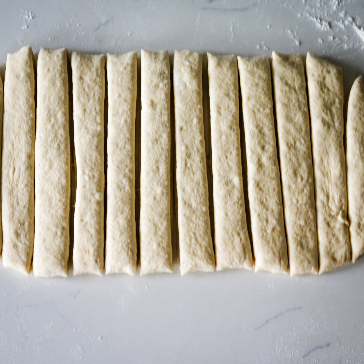 dough for pigs in a blanket on white counter cut up into thin vertical pieces.