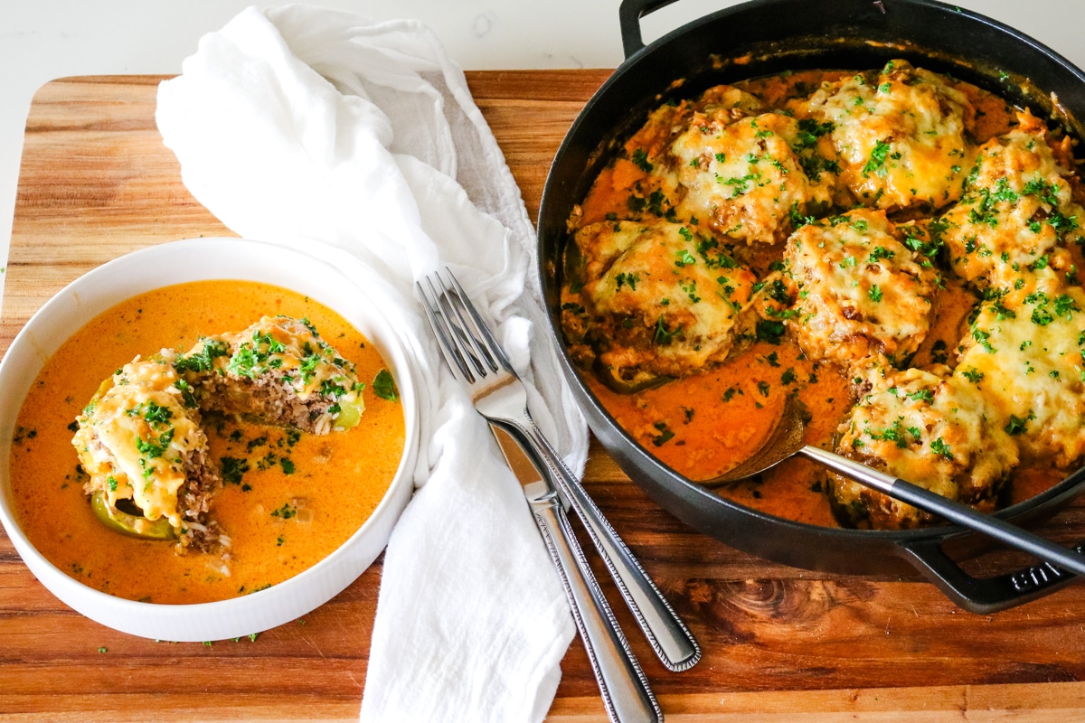 smothered stuffed bell peppers in a deep dish with a single serving on the side and serving utensils.