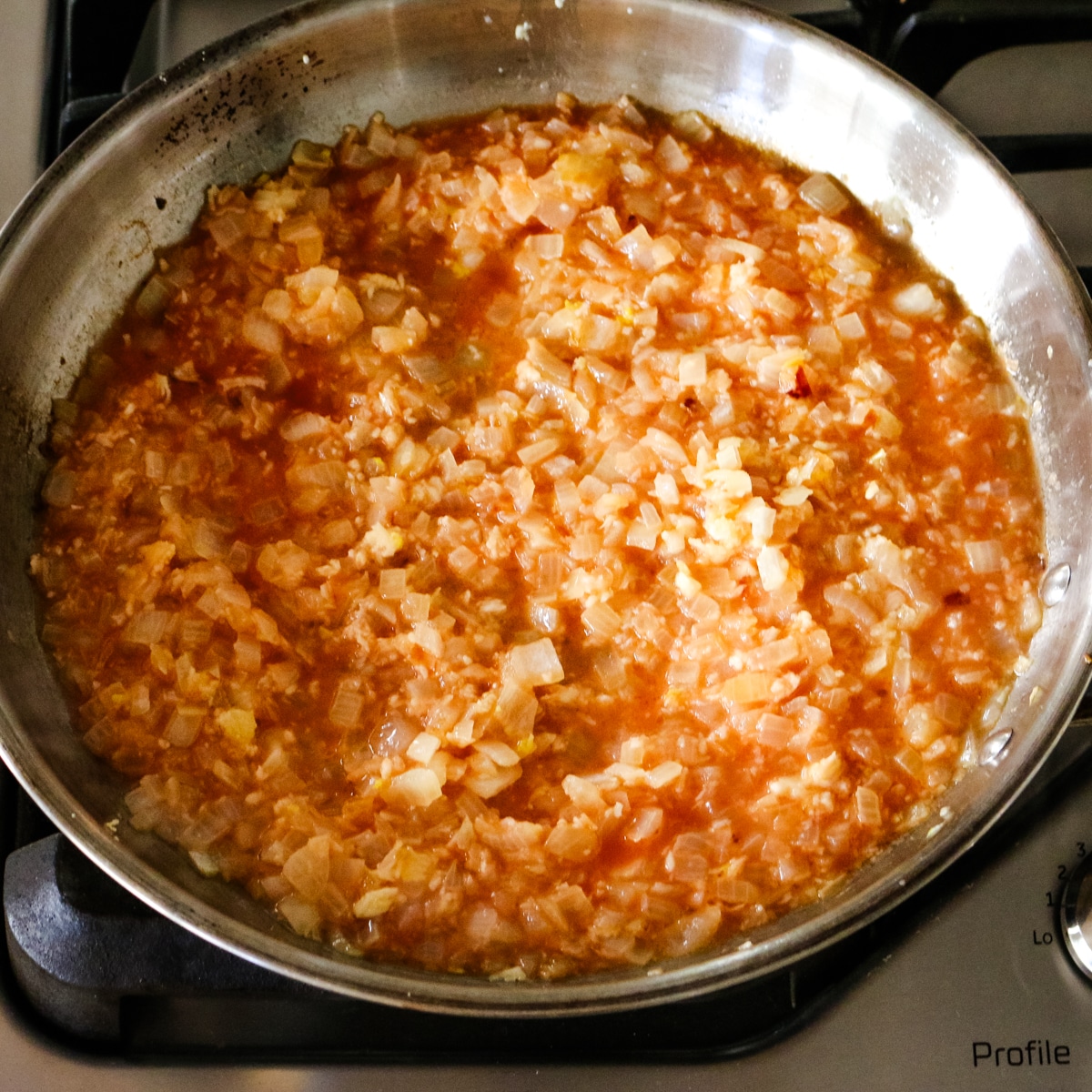 sauteed onions with tomato mixture in a stainless steel pan.