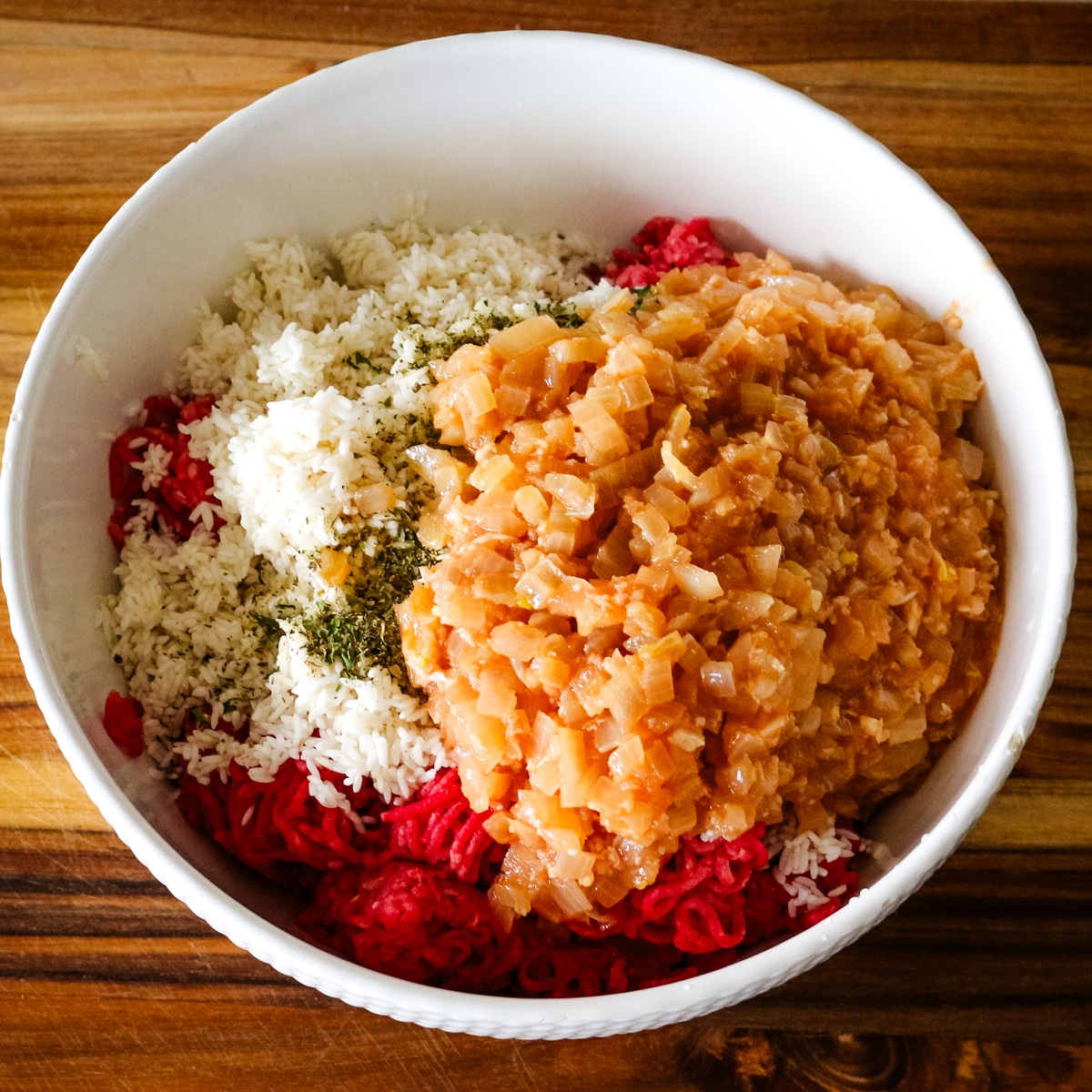a white bowl of ground beef, white rice, seasoning, and sauteed onions with tomato mixture.