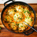 stuffed bell peppers in a creamy tomato sauce in a deep dish pan.