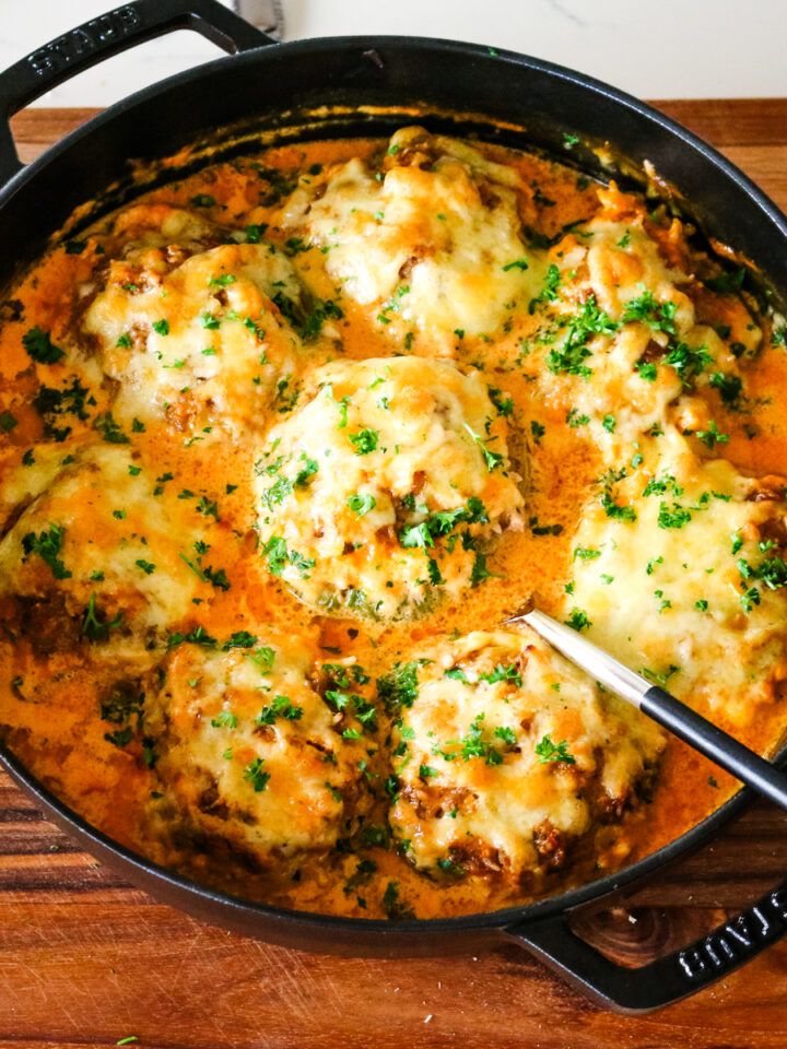 stuffed bell peppers in a creamy tomato sauce in a deep dish pan.