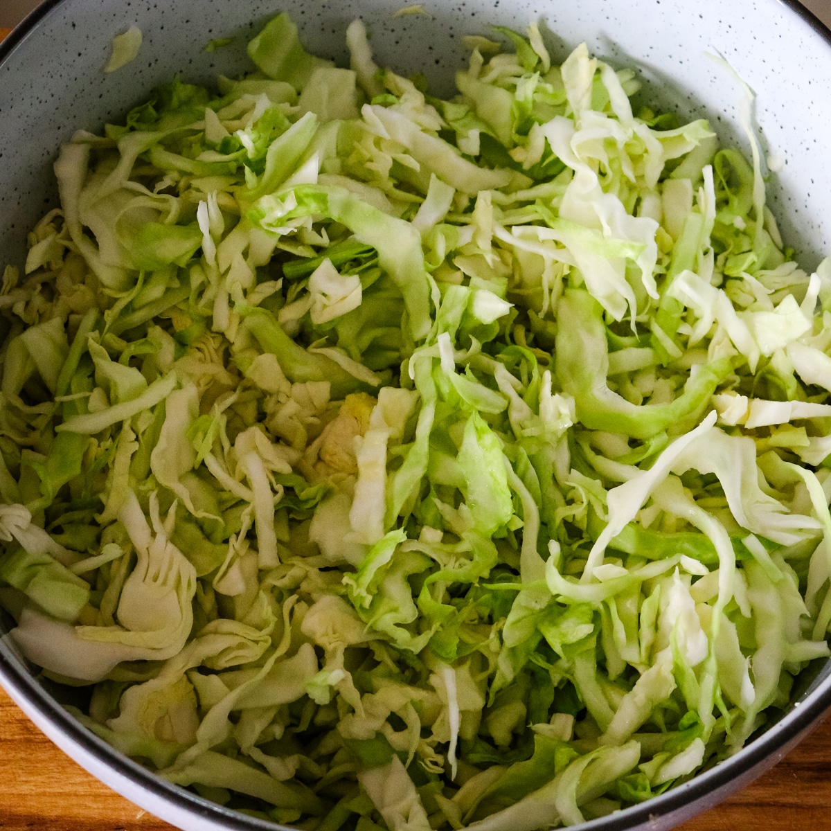 Finely shredded cabbage placed inside a large speckled mixing bowl, ready to be tossed into a salad.