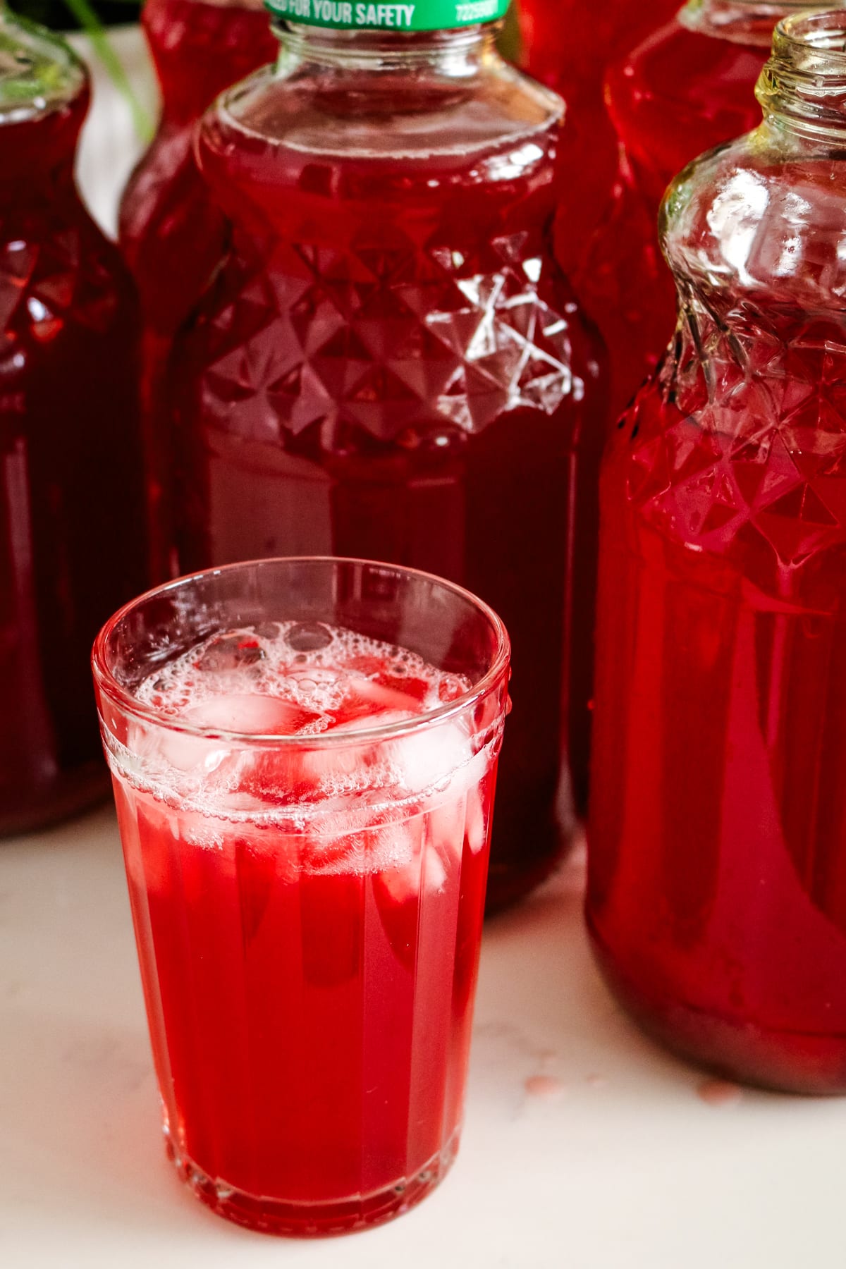 Iced homemade kompot in a glass next to jars filled with the beverage.