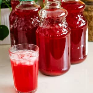 A glass of homemade fruit kompot, with several large glass jars filled with the beverage.