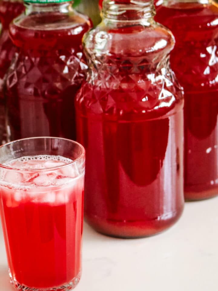 A glass of homemade fruit kompot, with several large glass jars filled with the beverage.