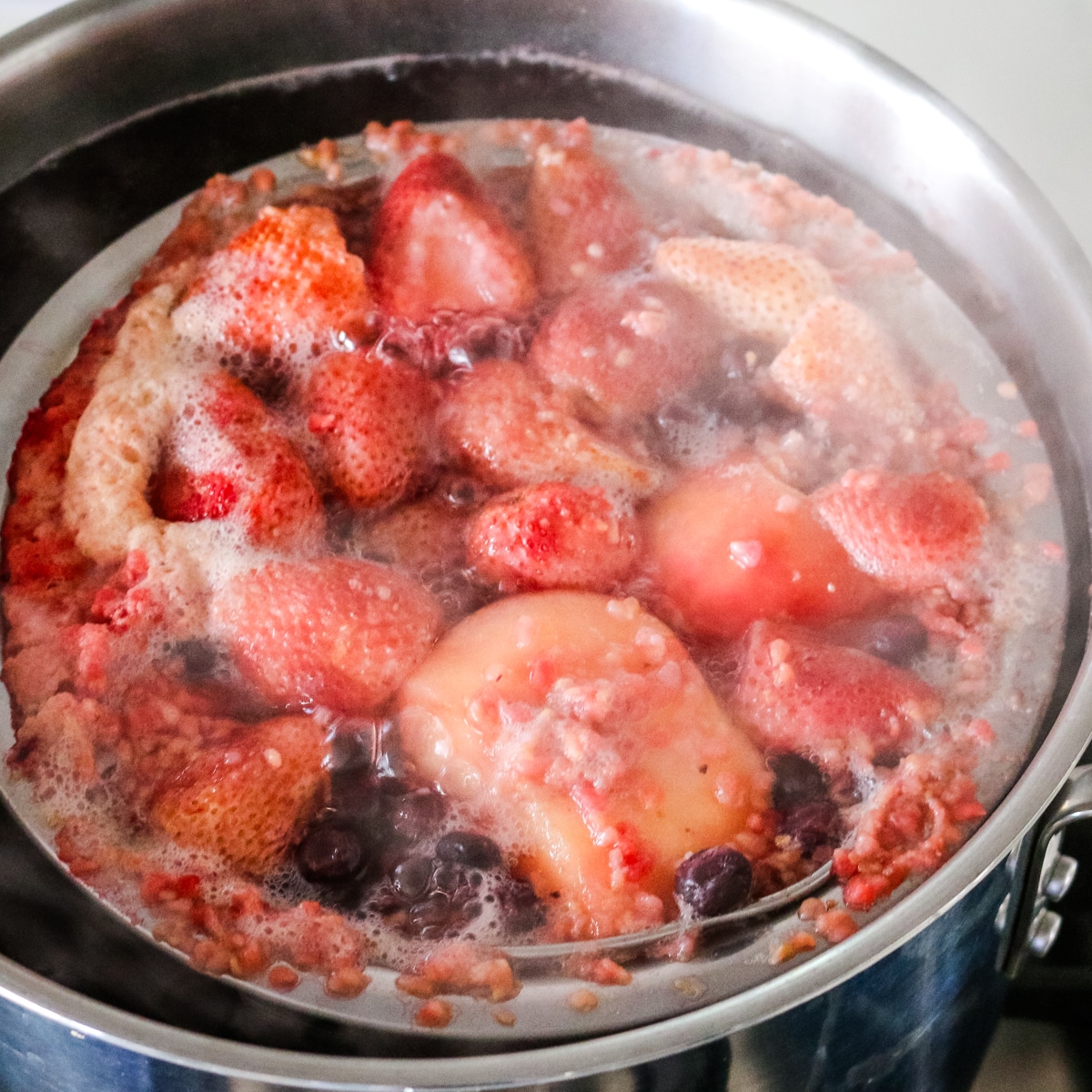 Mixed fruit simmering in a pot of water for kompot.