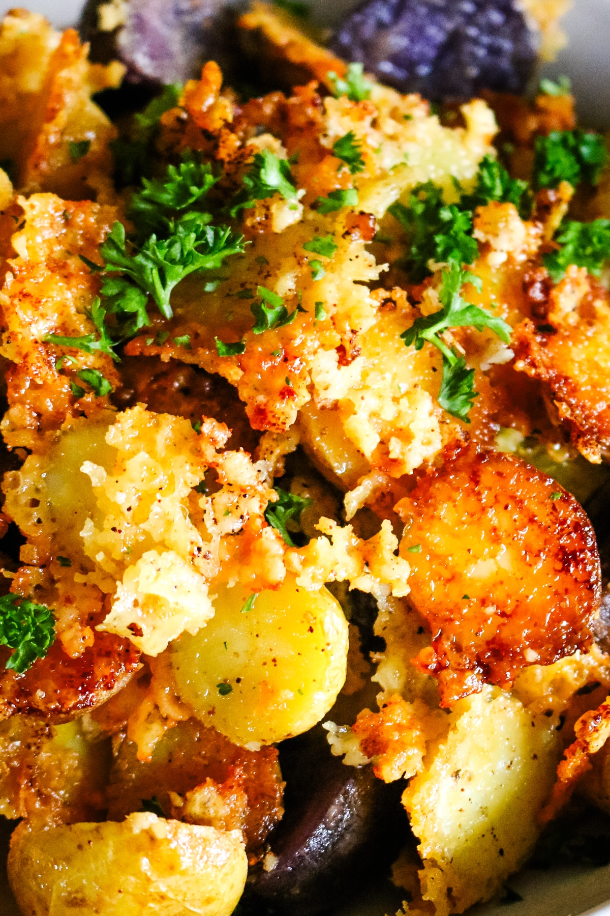 Close up of crispy, golden parmesan crusted potatoes garnished with fresh chopped parsley.