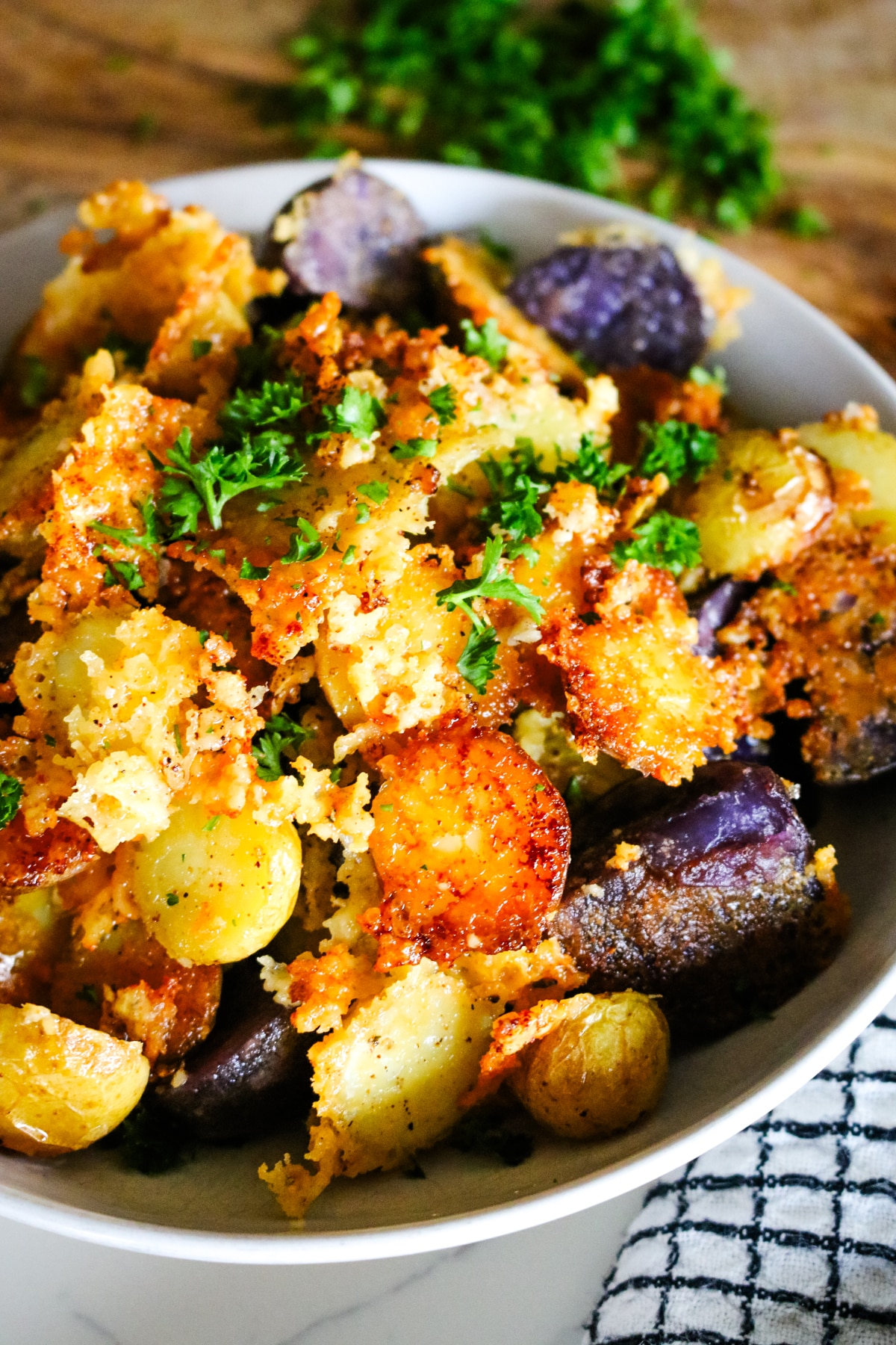 Parmesan crusted potatoes in a white bowl, with chopped parsley on a cutting board in the background.