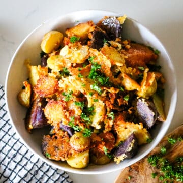 parmesan crusted potatoes in a white bowl, garnished with fresh parsley.
