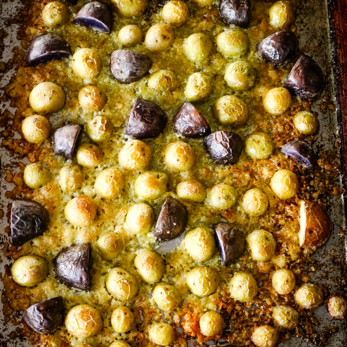 Golden brown roasted potatoes on a metal baking sheet, topped with melted, bubbly parmesan cheese.