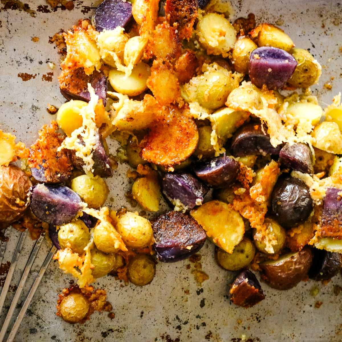 A metal spatula scoops crispy parmesan crusted roasted potatoes off a metal baking sheet.