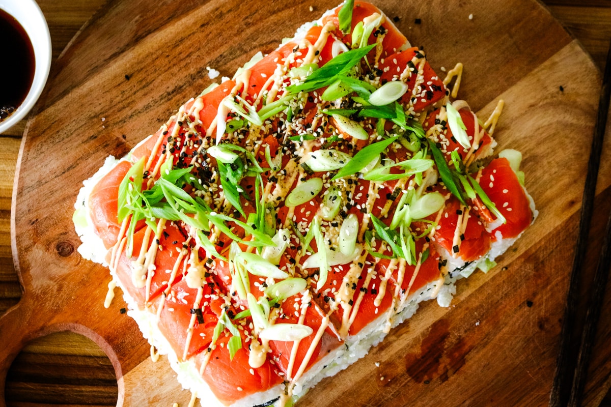 smoked salmon sushi with rice, green onions, and a bowl of soysauce on the side.