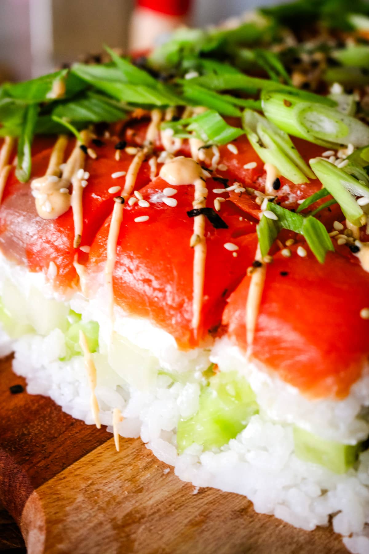 close up shot of smoked salmon sushi with rice, green onions, and spicy mayo drizzled on top.