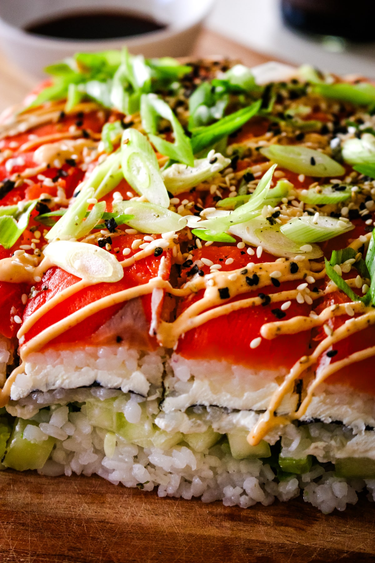 smoked salmon sushi with rice, green onions, and a bowl of soy sauce in the backround.
