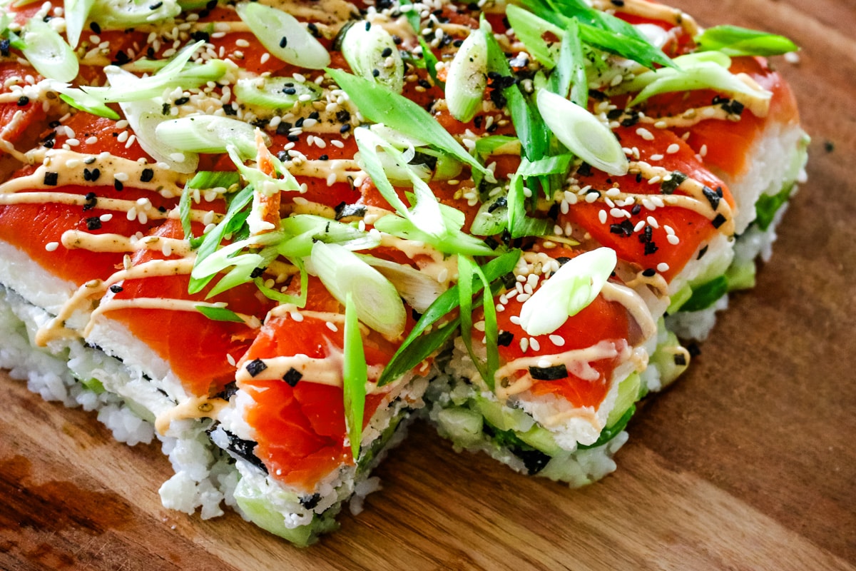 close up shot of smoked salmon sushi with rice, green onions, and spicy mayo drizzled on top.