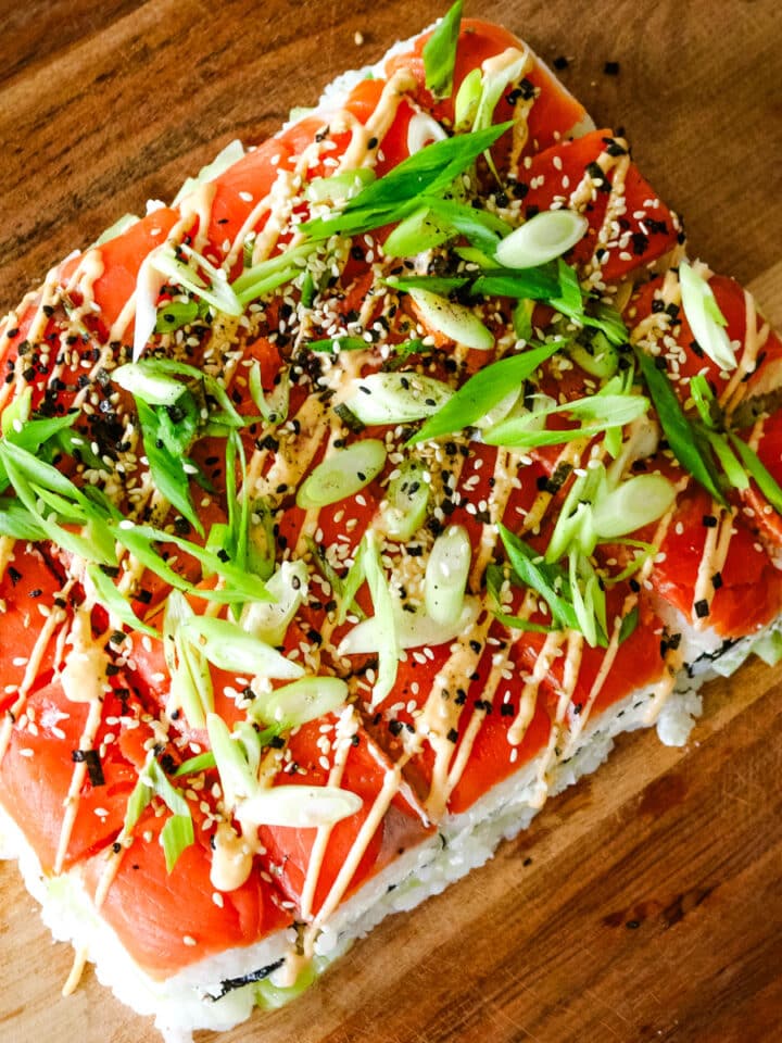 smoked salmon sushi with rice, green onions, and spicy mayo drizzled on top.