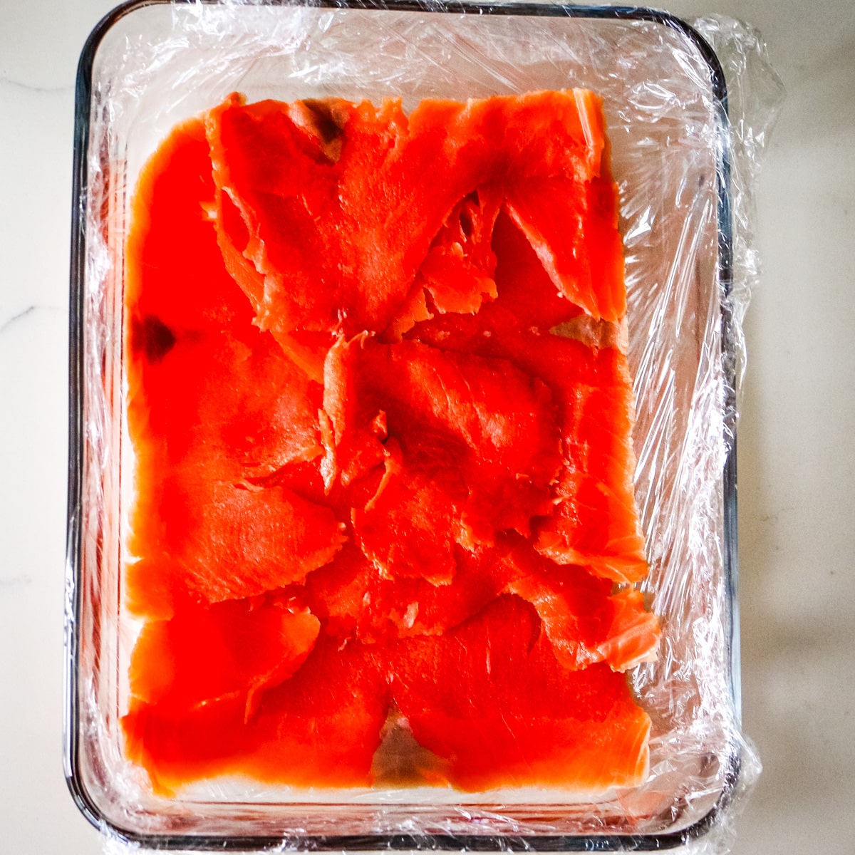 smoked salmon on top of rice, in a glass container.