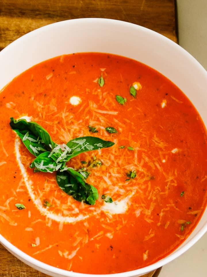 A bowl of homemade tomato bisque topped with fresh basil leaves and shredded parmesan cheese next to grilled sourdough.