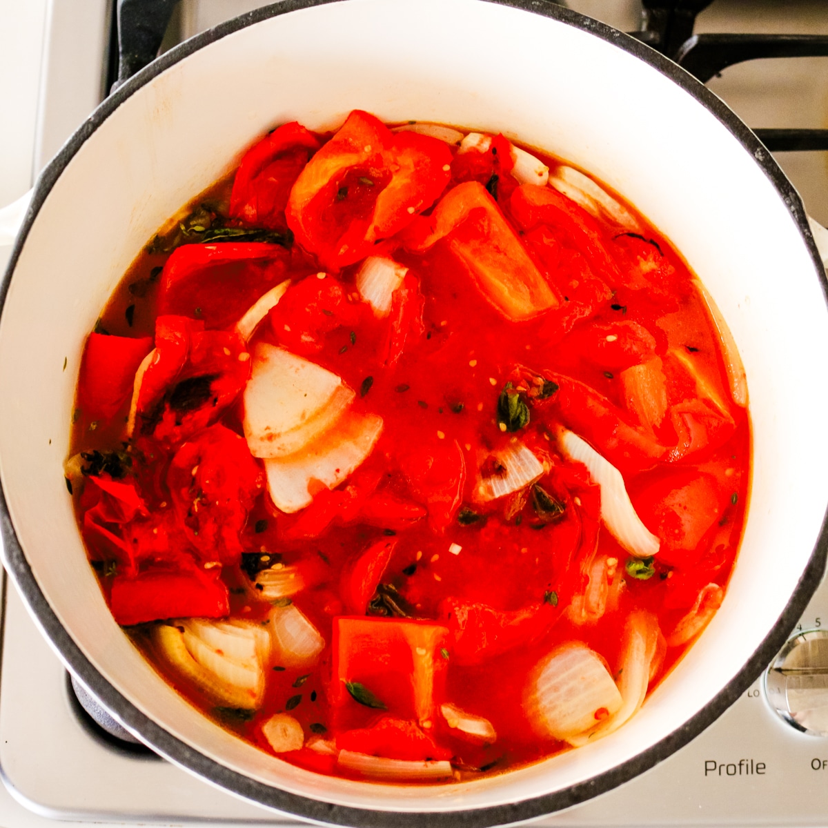 Sautéed tomatoes, onions, garlic, and fresh herbs simmering in broth inside a Dutch oven before blending into tomato bisque.