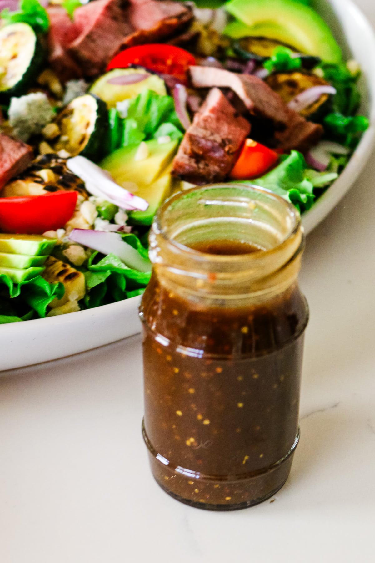 homemade balsamic vinaigrette dressing in a glass jar in front of bowl of salad.