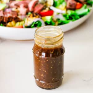 homemade balsamic vinaigrette dressing in a jar sitting in front of a bowl full of salad.