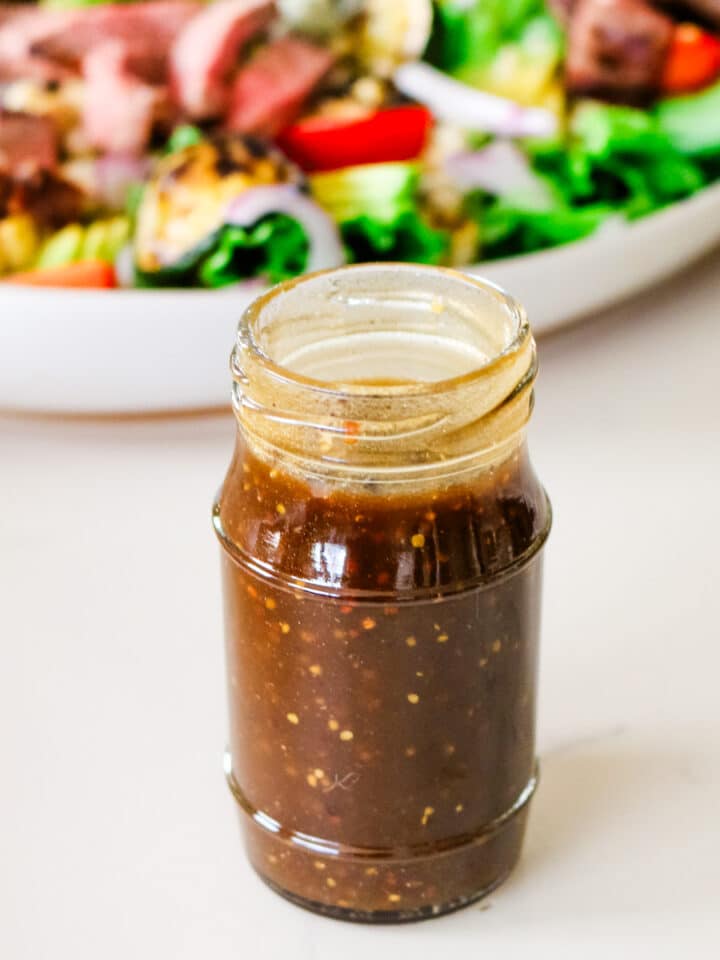 homemade balsamic vinaigrette dressing in a jar sitting in front of a bowl full of salad.