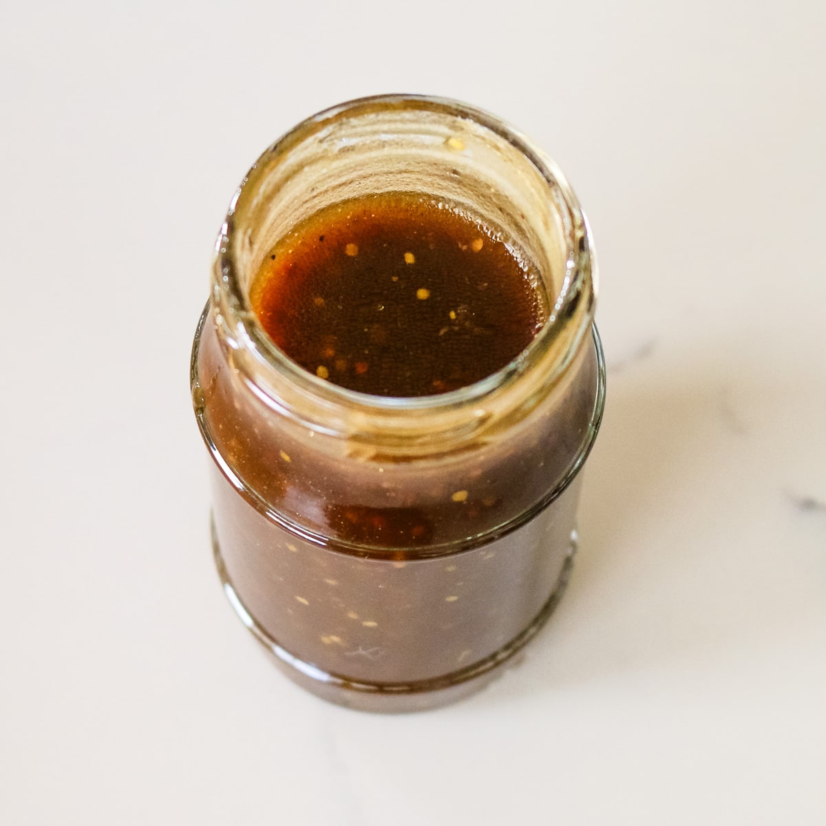 homemade balsamic vinaigrette dressing in a glass jar on a marble countertop.