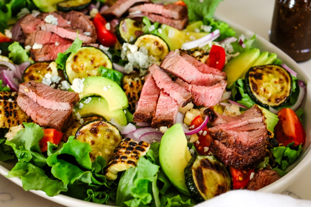 photo of steak salad in a white bowl with a jar of vinaigrette on the side.