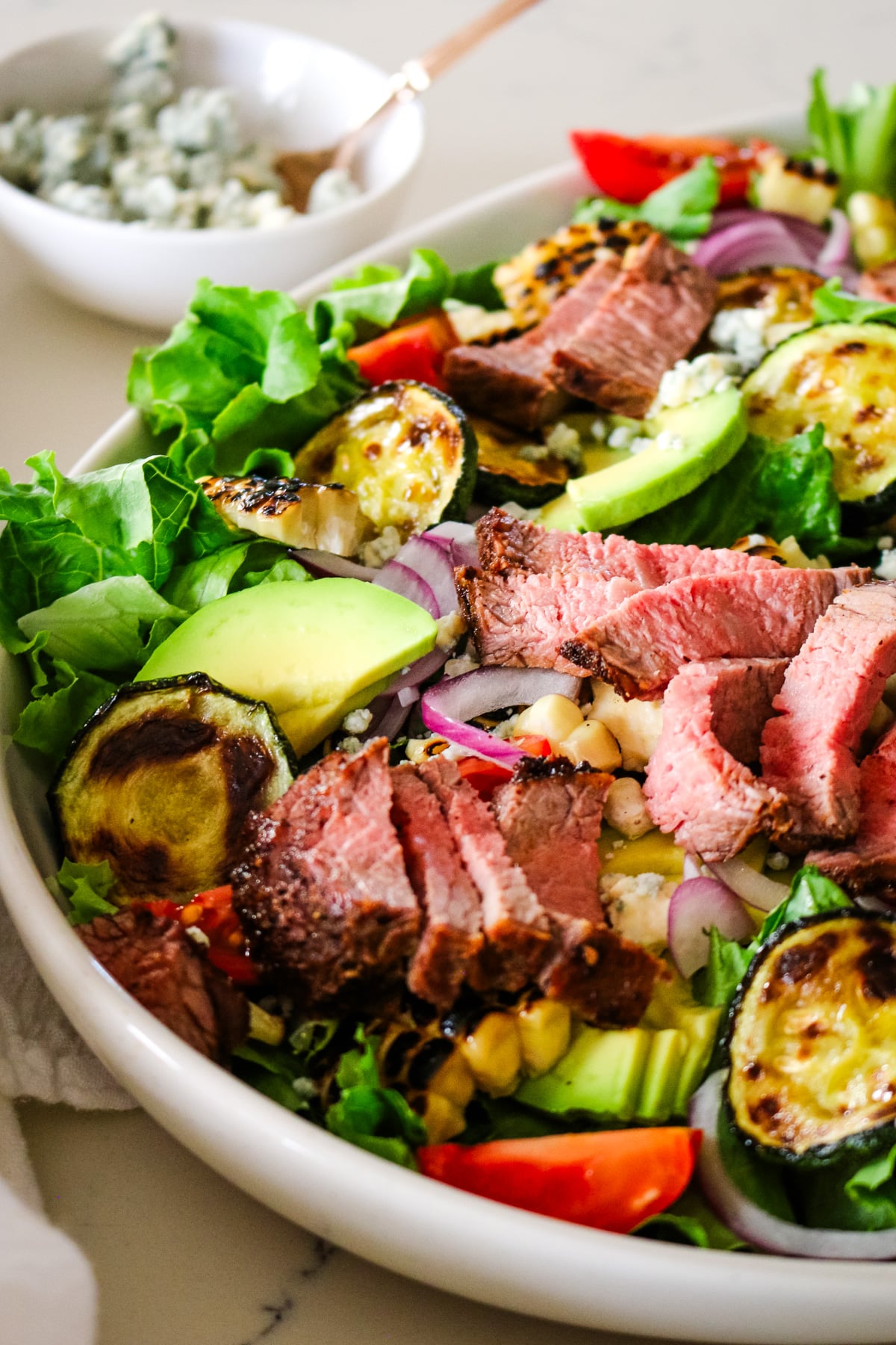 photo of steak salad in a white bowl with a little bowl of blue cheese on the side.