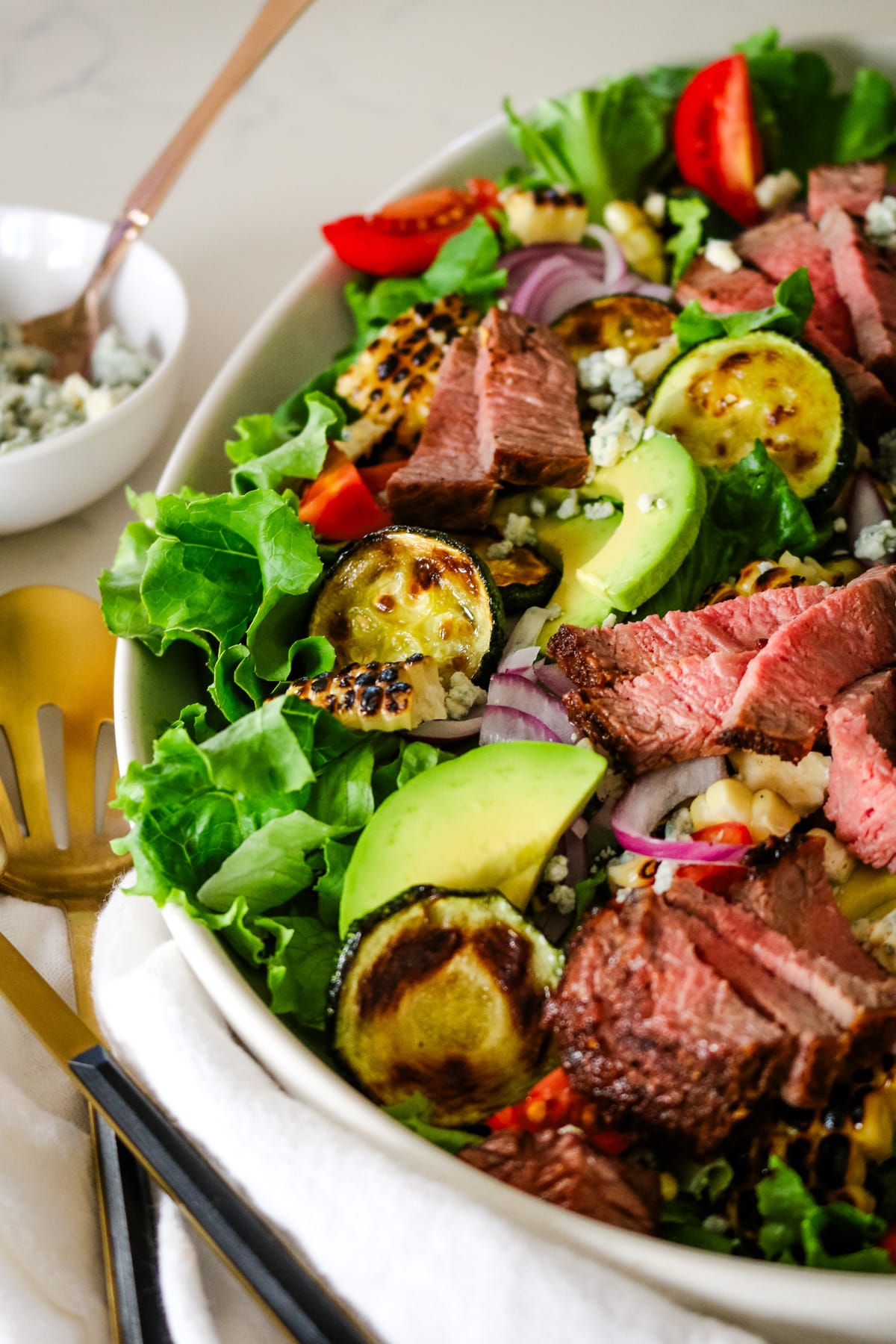 photo of steak salad in a white bowl with a little bowl of blue cheese on the side..