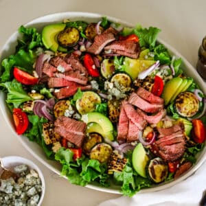 photo of steak salad in a white bowl with a little bowl of blue cheese on the side.