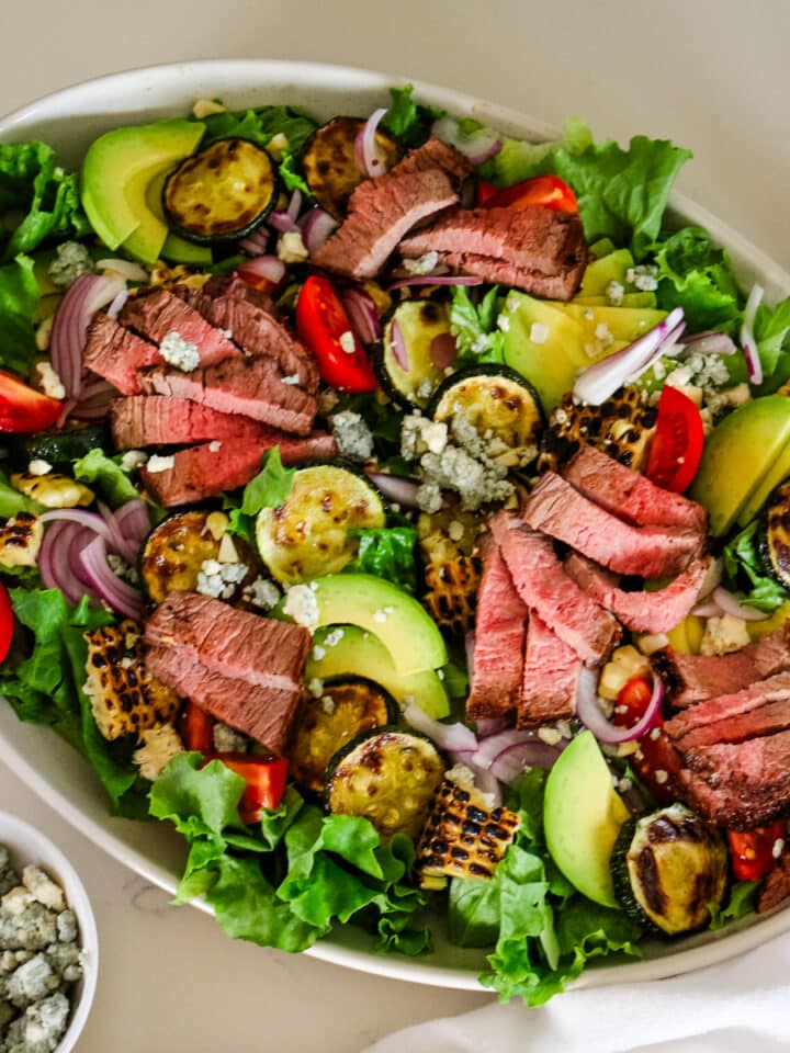 photo of steak salad in a white bowl with a little bowl of blue cheese on the side.