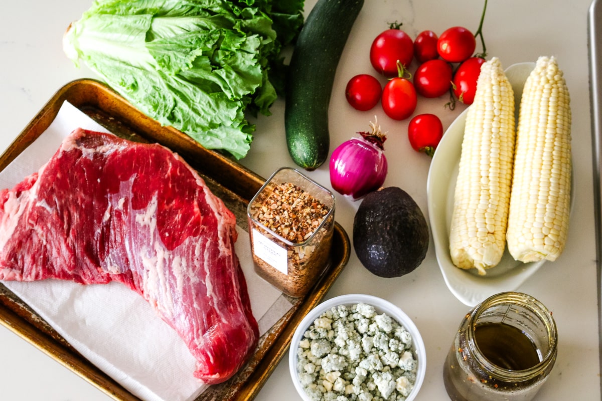 photo of all ingredients needed to make steak salad (including steak, lettuce, tomatoes, corn).
